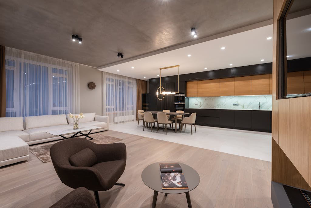 Modern studio interior with armchair near couch and tables with chairs under lamps next to open kitchen and TV on wall